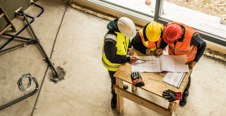 Trade workers huddle to evaluate construction blueprints.