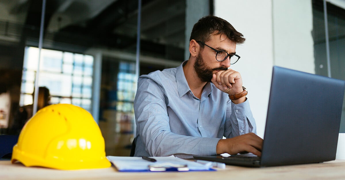 A construction professional in a modern office is deeply focused while working on a laptop.