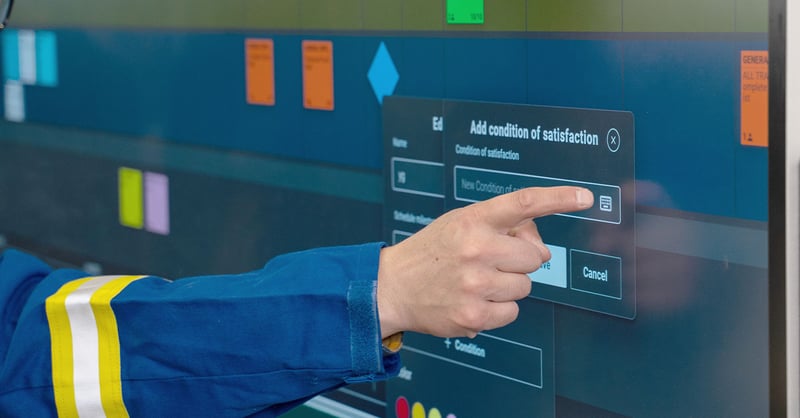 Nialli Visual Planner is shown on a large screen. One hand is shown touching the screen to add "condition of satisfaction"