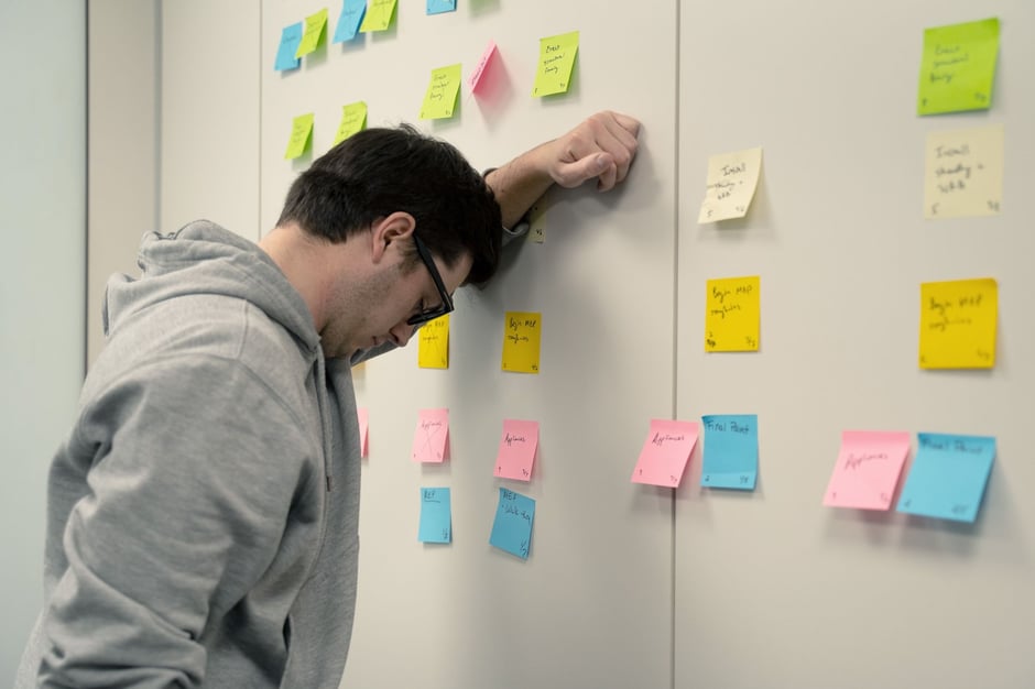 Frustrated construction worker using sticky notes to plan tasks on a wall.