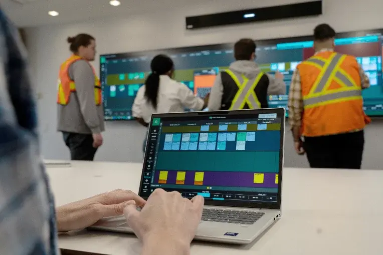 Multiple users collaborate using Nialli Visual Planner, with one individual using a laptop and multiple individuals collaborating on a interactive display.